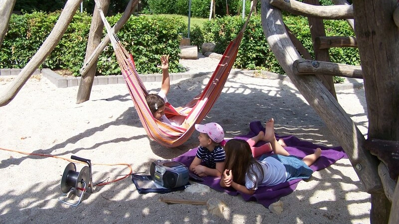 Kinder liegen in der Hängematte und hören im Kies Musik